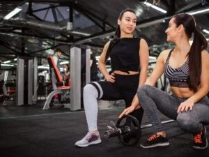 "Beautiful young asian woman stand on one knee and look at her friend. She holds one hand on her leg. She youches weight."